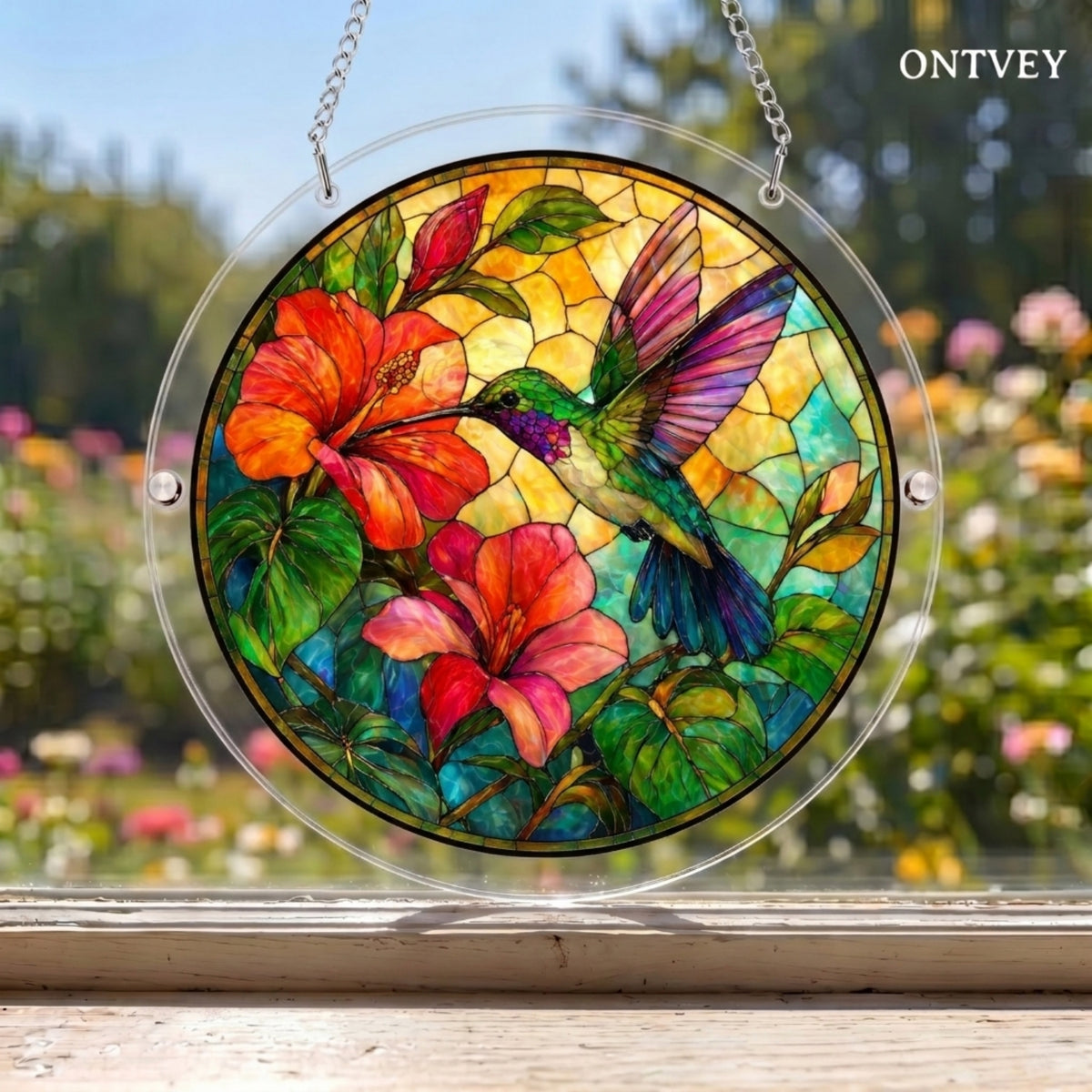 Hummingbird puzzle suncatcher hanging in a window with a garden behind it