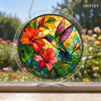 Hummingbird puzzle suncatcher hanging in a window with a garden behind it